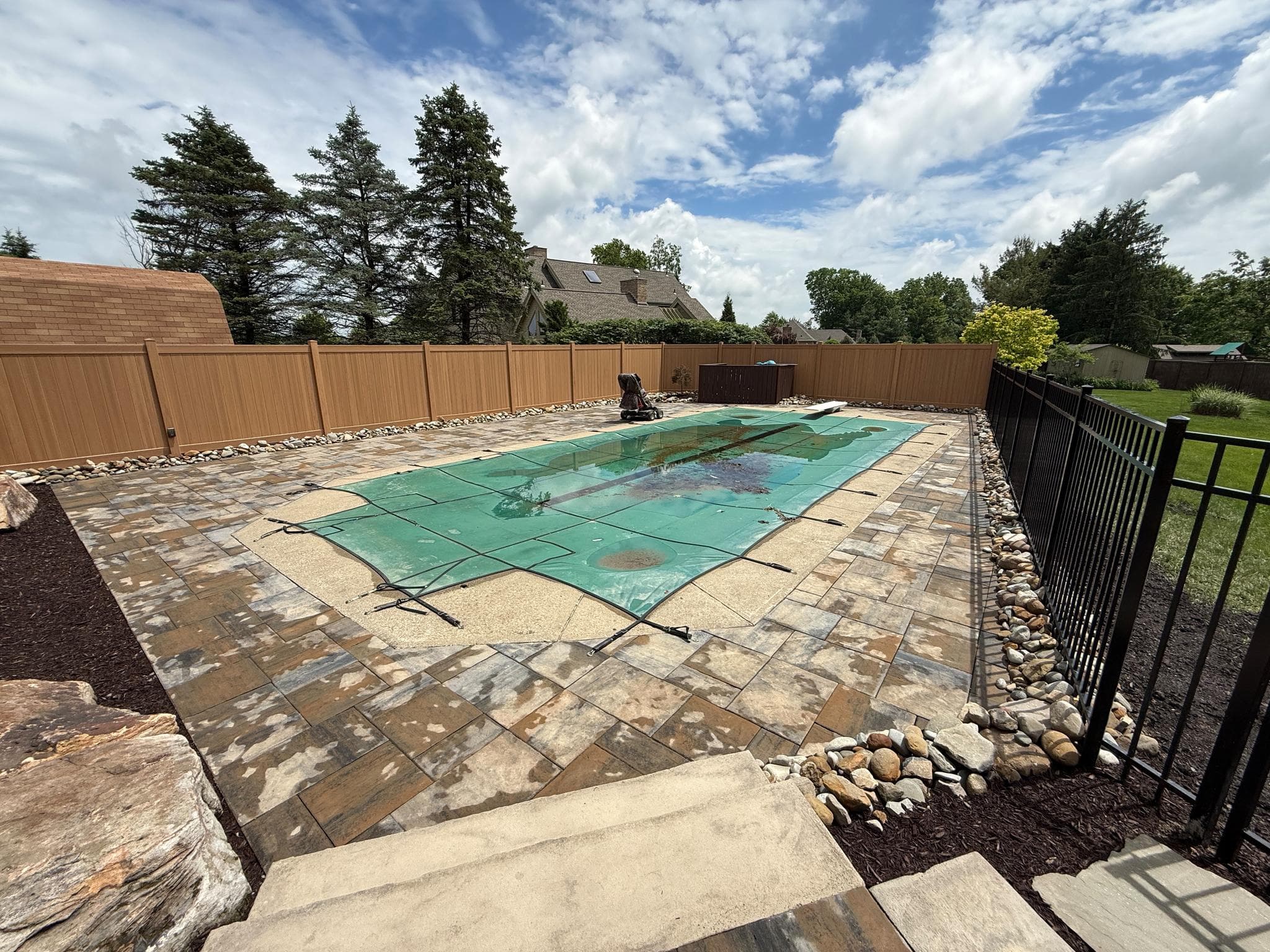 Pool and patio fence installation in Pittsburgh with paver decking, black aluminum pool fence, and cedar-tone vinyl privacy fence