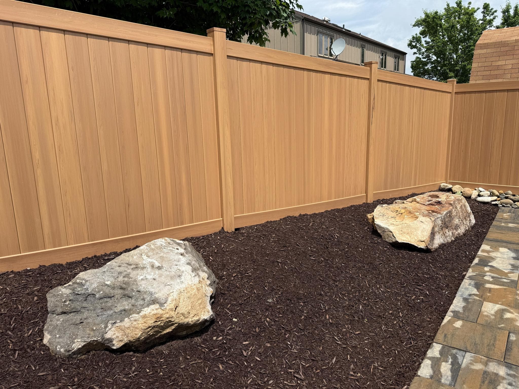Paver pool patio installation framed by a cedar-tone vinyl privacy fence in Pittsburgh