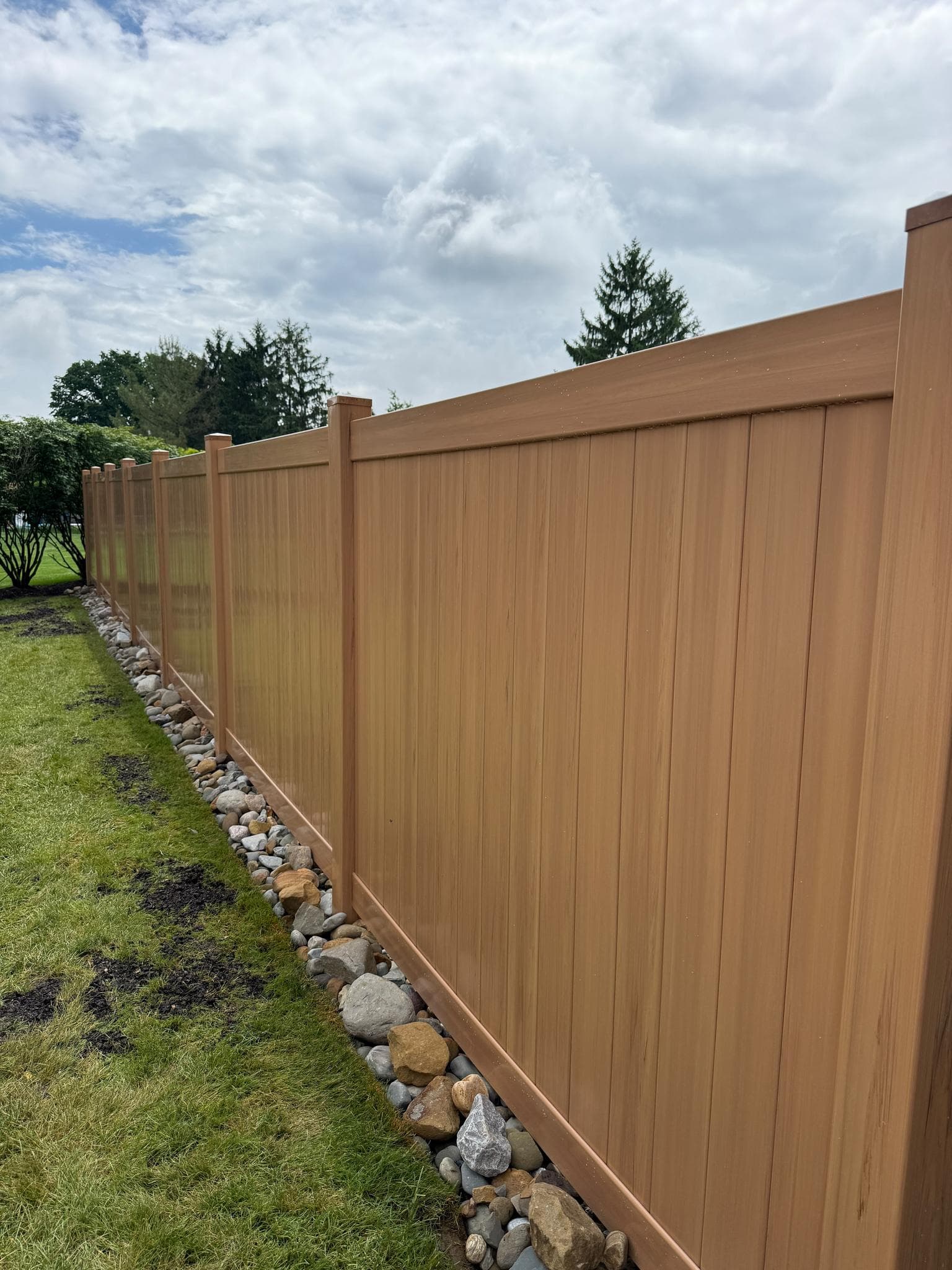 Vinyl privacy fence with a river-rock drainage border in Pittsburgh